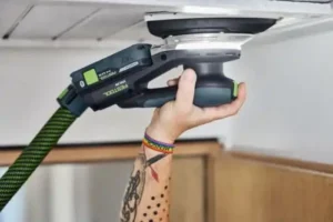 Akku-Deltaschleifer-DTSC200-im-Einsatz Festool Deltaschleifer DTSC 200 LED-Leuchte und Absaugschlauch bei Schleifen einer weißen Holzdecke.